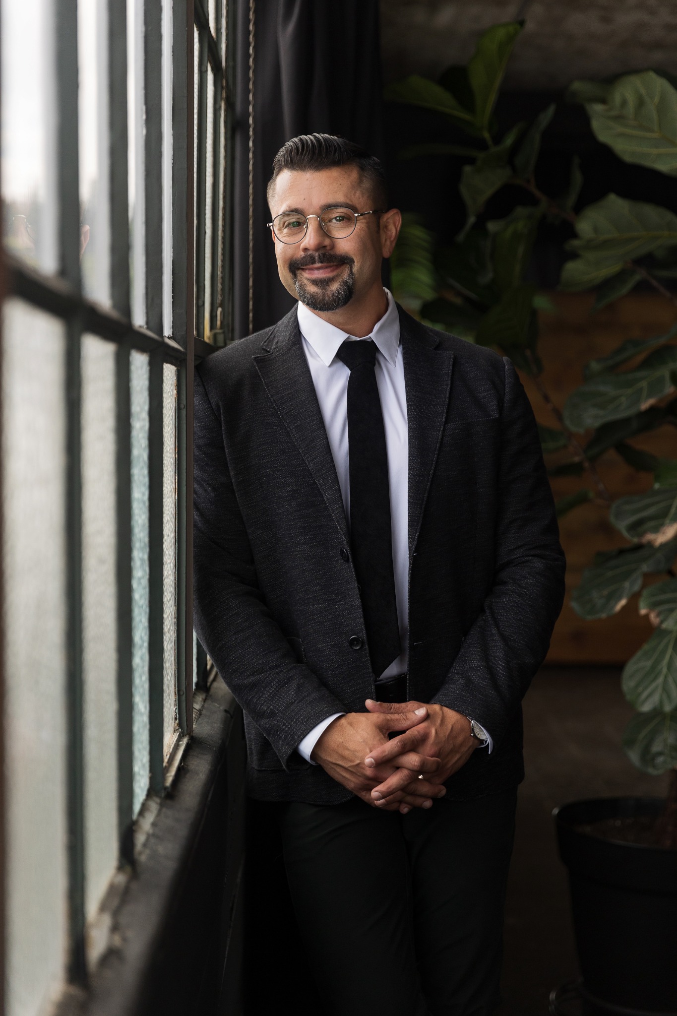 Enrique Pelayo Jr. in a dark suit beside tall windows